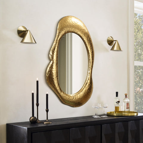 free form shaped metal wall mirror above a black console cabinet. two gold color wall sconce on both sides of the mirror. Candle holders and decorative tray on top of the cabinet.