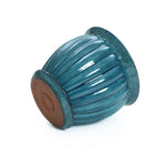 A navy blue glazed ceramic decorative planter lies on its side, showcasing a ribbed texture and round base with a brown bottom.