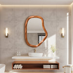 Modern bathroom featuring an asymmetrical wall mirror with a wood frame above a white sink.
