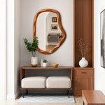 Modern entryway features an asymmetrical wall mirror, a wooden console table, two cushioned stools.