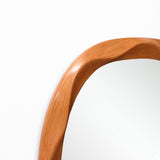 Close-up of the top an asymmetrical wall mirror with a smooth, wooden frame featuring a gentle wave-like contour.