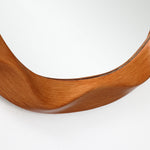 Close-up of the lower edge of an asymmetrical wood frame wall mirror with a smooth, curved design.