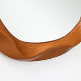 Close-up of the lower edge of an asymmetrical wood frame wall mirror with a smooth, curved design.