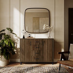 Mid-century walnut sideboard with drawers and plants on top stands against a beige wall with a large mirror.