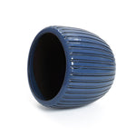 A dark blue, oval-shaped ceramic flowerpot with a three-dimensional vertical pattern lies on its side against a plain white background.