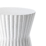 A close-up of the Speckled White Fluted Hourglass Outdoor Side Table reveals its rippled, speckled surface and vertical grooves. Crafted from durable MgO, the sleek design features a smooth tabletop that contrasts artistically with its cascading sides.