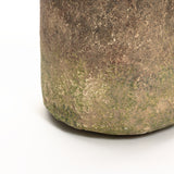 Close-up of the textured surface of a weathered, rustic vase with a ginger root brown finish, covered in moss, set against a white background.