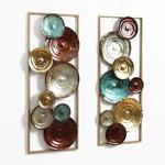 Two vertical decorative wall sculptures feature circular, textured discs in brown, teal, and gold tones, arranged within rectangular gold frames against a white background.