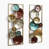 Two vertical decorative wall sculptures feature circular, textured discs in brown, teal, and gold tones, arranged within rectangular gold frames against a white background.
