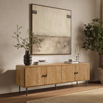 Minimalist TV stand with black legs stands against a beige wall, topped with books, candles, and a vase with branches.