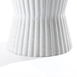 Close-up of a speckled white fluted hourglass outdoor side table made from MgO, featuring textured ribbed grooves. Its surface casts a soft shadow on a white background, offering a modern aesthetic.