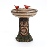 A captivating polyresin garden birdbath with a tree trunk base, featuring the wise face of a brown old man. Two cheerful red birds perch on the rim, making it an enchanting outdoor decor centerpiece.