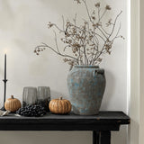 Black table a terracotta vase with dried branches brings vintage home decor charm against a light wall.