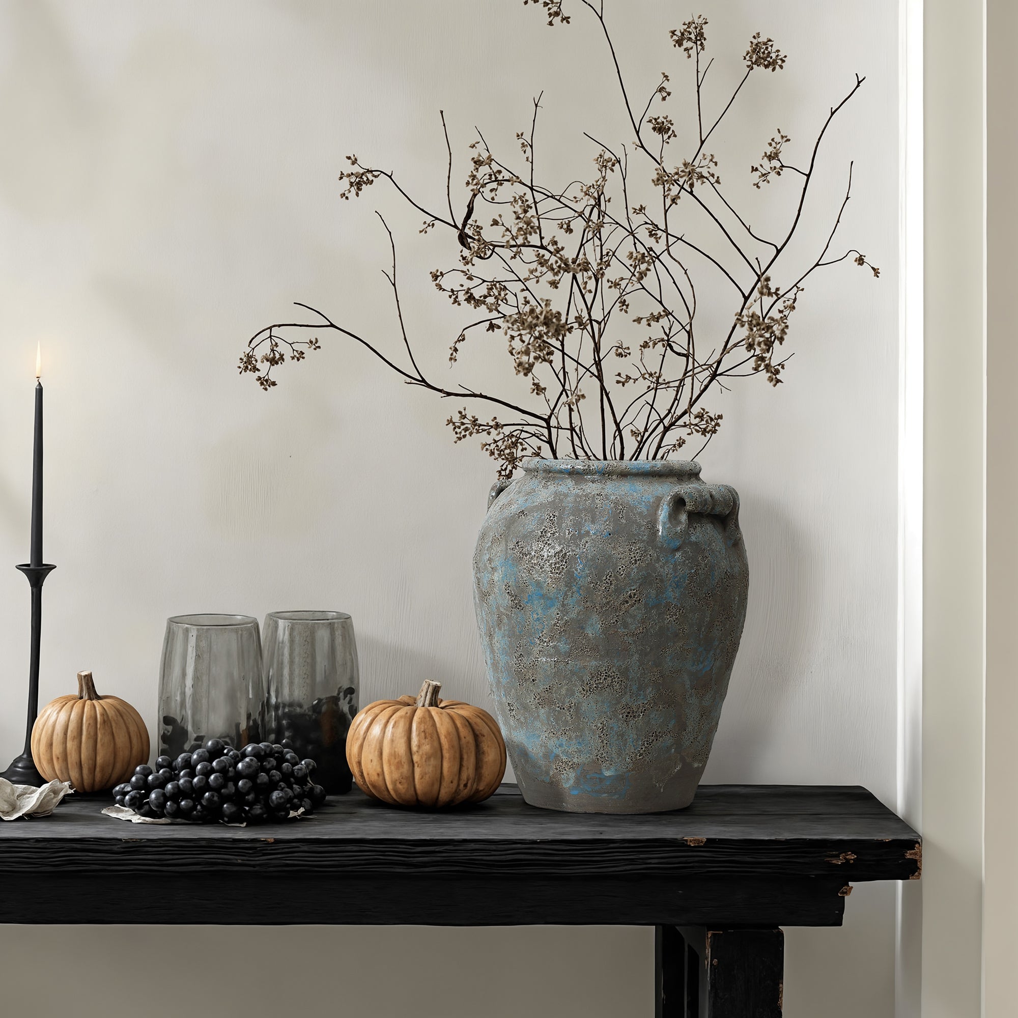 Black table a terracotta vase with dried branches brings vintage home decor charm against a light wall.