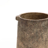 Close-up of a rustic vase with a weathered, cylindrical stone form and a small spout on one side, set against a plain white background.