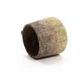 A weathered, cylindrical stone object with a rough texture, reminiscent of a rustic cement vase, rests on its side against a plain white background.