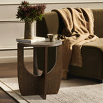 A mid-century modern side table with a walnut veneer holds a vase of flowers, a book, and a teacup. It sits elegantly beside a green sofa adorned with a draped brown blanket.