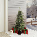 Small potted slim christmas tree is surrounded by 3 red gift boxes with green ribbons, white rabbit figurine on snowy porch.