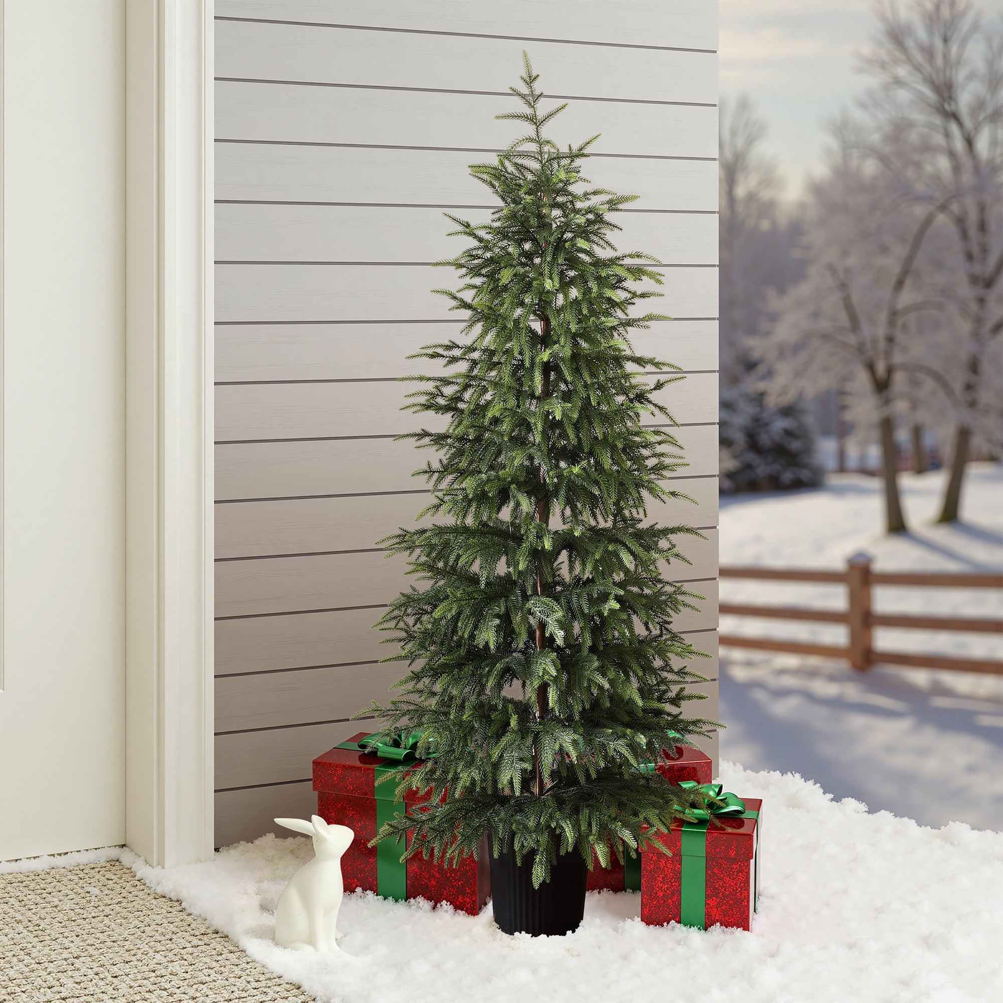 4ft artificial fir tree sits on snow by wall, flanked by red gift boxes with green bows, white rabbit figurine; snowy trees.background.