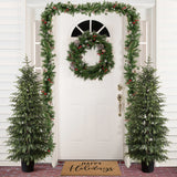 White front door decor with wreath, garland is flanked by 2 4ft artificial christmas fir trees, a doormat reading “Happy Holidays.”.