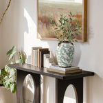 A decorative console table with books, white bookends, and a round floral ceramic vase with foliage.
