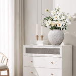 A white dresser with round cement flower vase filled with white blooms in a bright minimal room with.