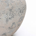 A close-up view of a textured, grayish-brown stone surface with scattered dark speckles against.