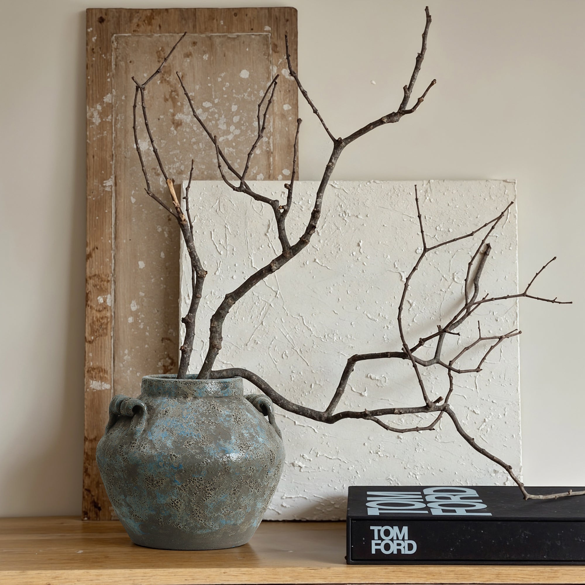 Handcrafted terracotta vase with bare branches sits on a wooden surface next to stacked books.