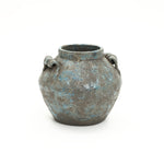 A round weathered terracotta vase with a blue-green patina, two handles on each side, and a wide opening.