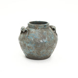 A round weathered terracotta vase with a blue-green patina, two handles on each side, and a wide opening.