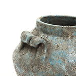 Close-up of a handcrafted vase with a rounded shape, blue and gray glaze, and a decorative handle detail near the rim.