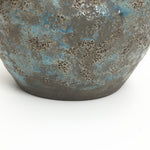 Close-up of the lower portion of a handcrafted vase with a rough, gray and blue-speckled surface.
