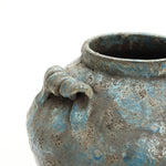 Close-up of a handcrafted pottery piece—an aged, textured ceramic pot with a blue and gray mottled surface.