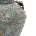 Close-up of a weathered handcrafted pottery vase with a rough, textured surface and a handle on the right side.