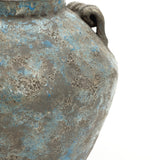 Close-up of a weathered handcrafted pottery vase with a rough, textured surface and a handle on the right side.