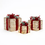 3 gold, textured gift boxes with red ribbons, artificial pine sprigs,red berries are displayed against white background.
