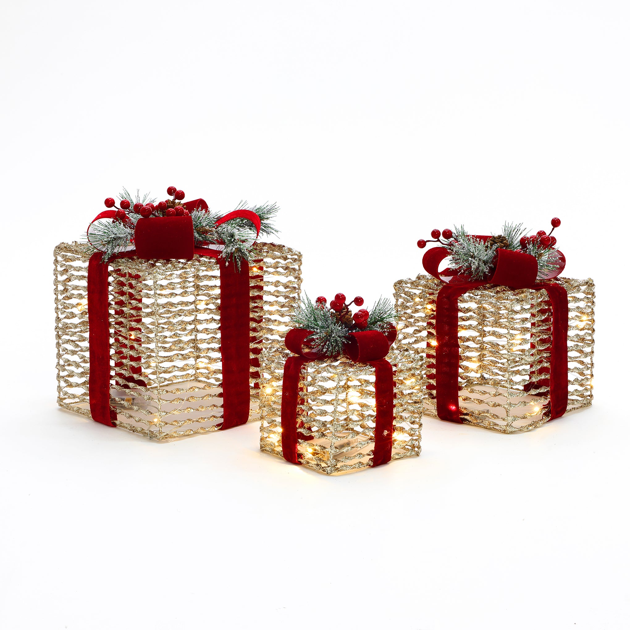 3 gold, textured gift boxes with red ribbons, artificial pine sprigs,red berries are displayed against white background.