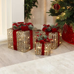 3 decor christmas presents with gold textured wrapping, red ribbons, greenery, led lights, sit on the floor beside.