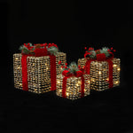 3 illuminated decor gift boxes with red ribbons, pine branches, red berries against a black background.