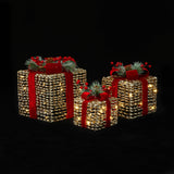 3 illuminated decor gift boxes with red ribbons, pine branches, red berries against a black background.