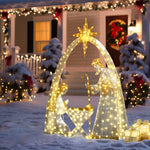 Pre-lit outdoor nativity scene with Mary, Joseph, baby Jesus stands on snow in front of house adorned with christmas decor,wreaths.