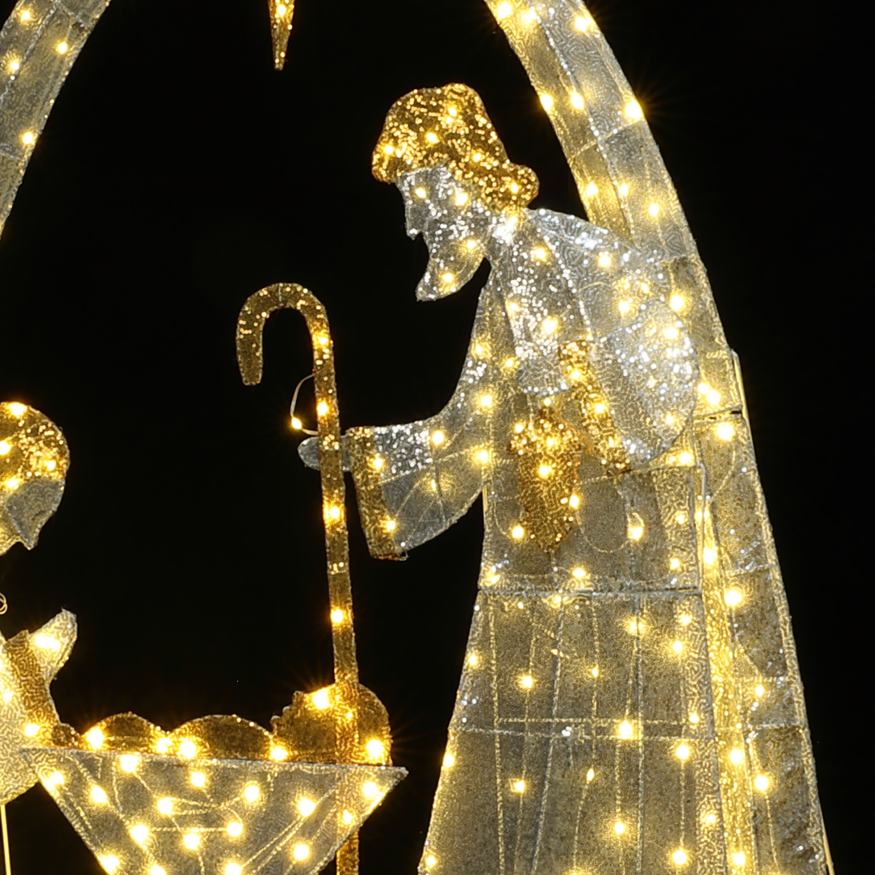 Outdoor holiday decor nativity scene features illuminated depicting a figure withstaff beside a manger.
