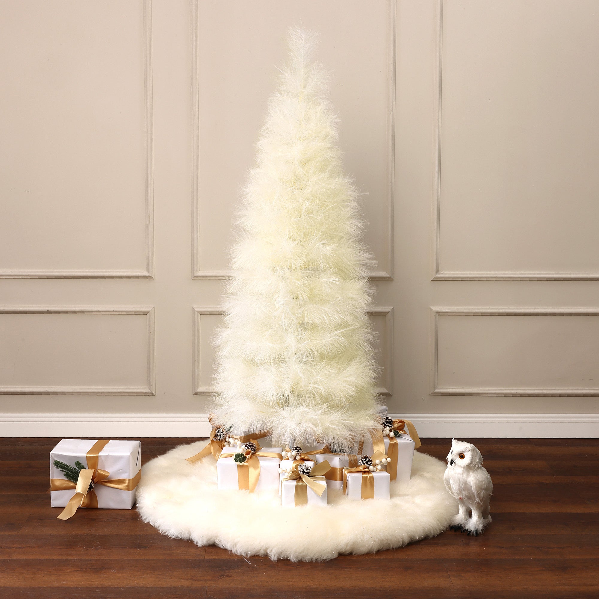White christmas tree, styled with natural artistic touch, stands atop white rug, gold, white wrapped gifts at base,decor white owl on the right.