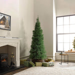 Artificial pampas grass tree stands in corner beside wrapped gifts, near fireplace, large window in bright living room.