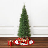 Slim 6ft pampas grass artificial christmas tree stands on white, red tree skirt with wrapped gifts beneath, against white paneled wall.