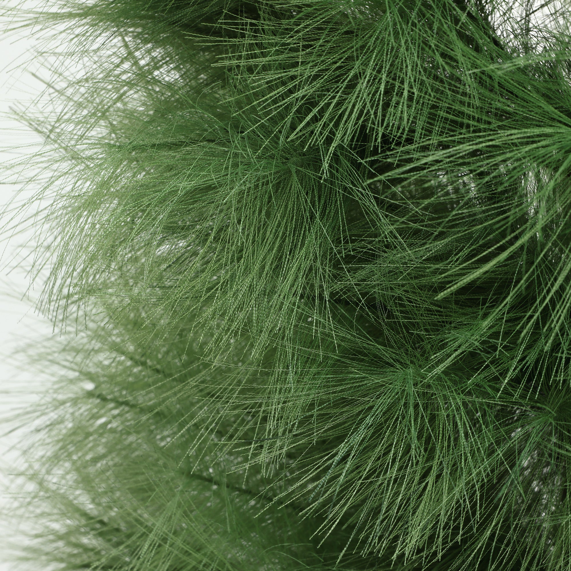 Close-up view of artificial christmas tree branches with fine, needle-like green leaves, against a plain background.