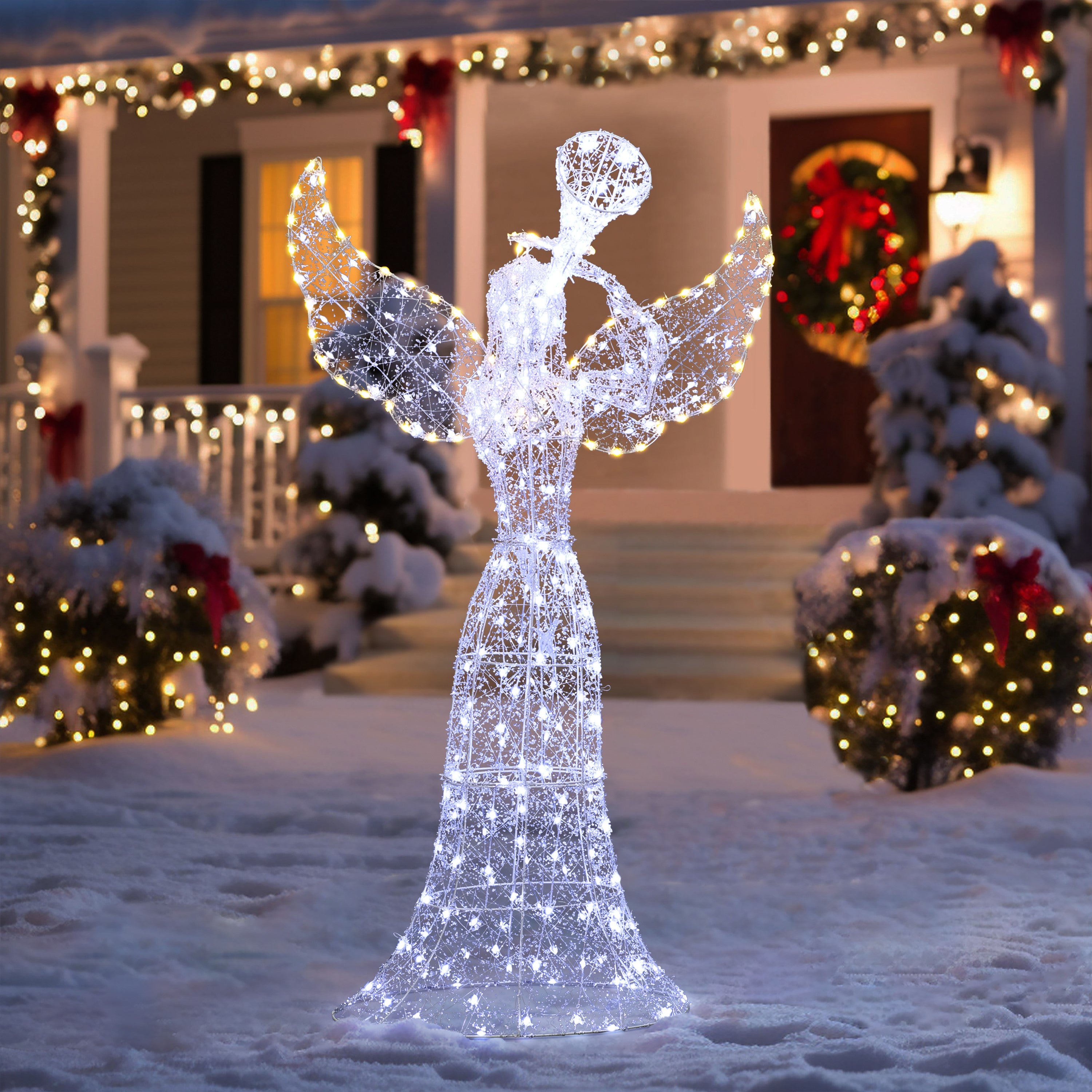 Wireframe angel outdoor decor glows on the snowy lawn, set before house adorned with lights, festive wreaths.