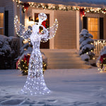 Lit christmas angel decor stands in the snow in front of house adorned with outdoor holiday lights ,wreaths.