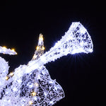 Wireframe christmas angel decor plays a trumpet, illuminated by white outdoor holiday against the black night sky.