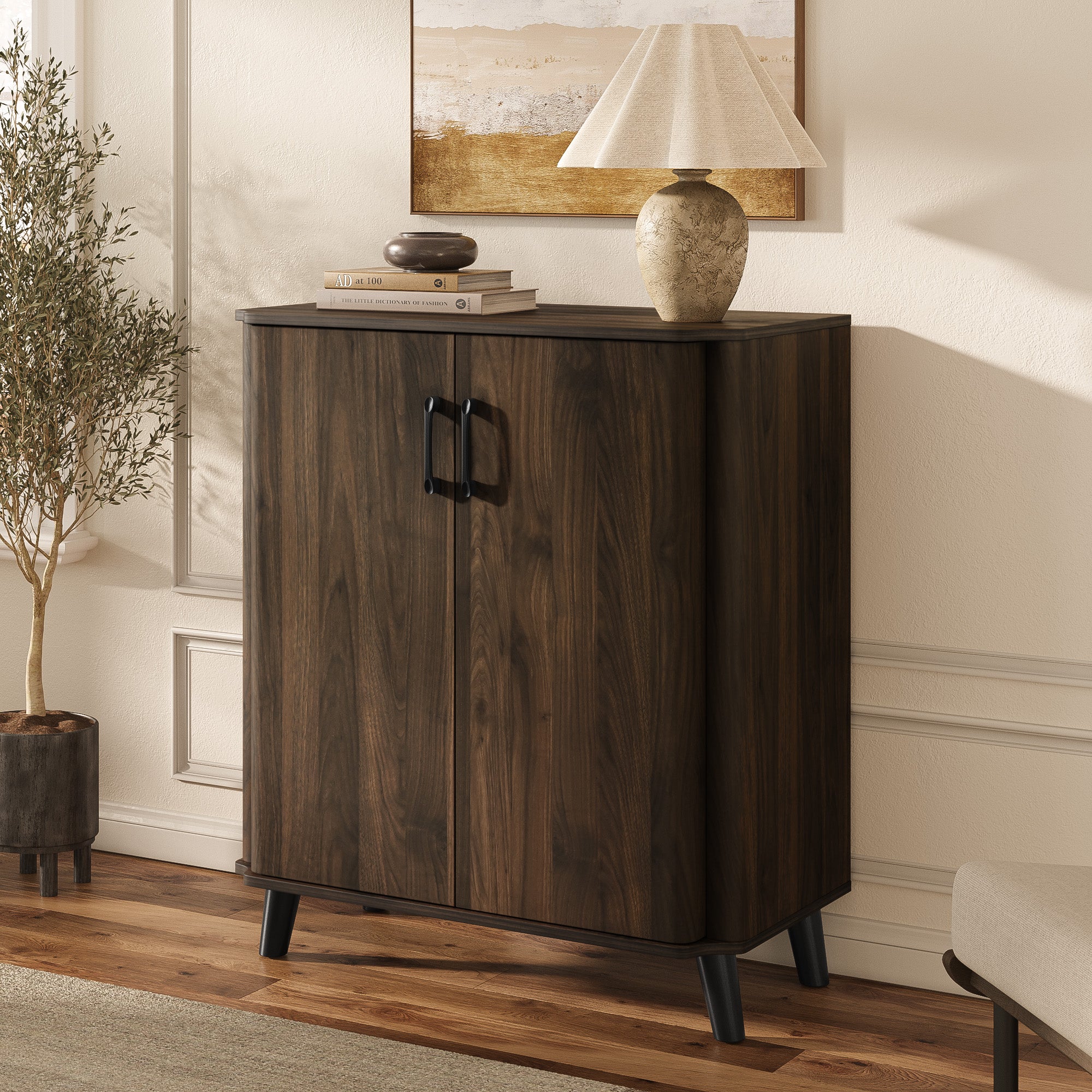 Mid-century sideboard cabinet with black handles stands against a wall, topped with a beige table lamp, two stacked books.